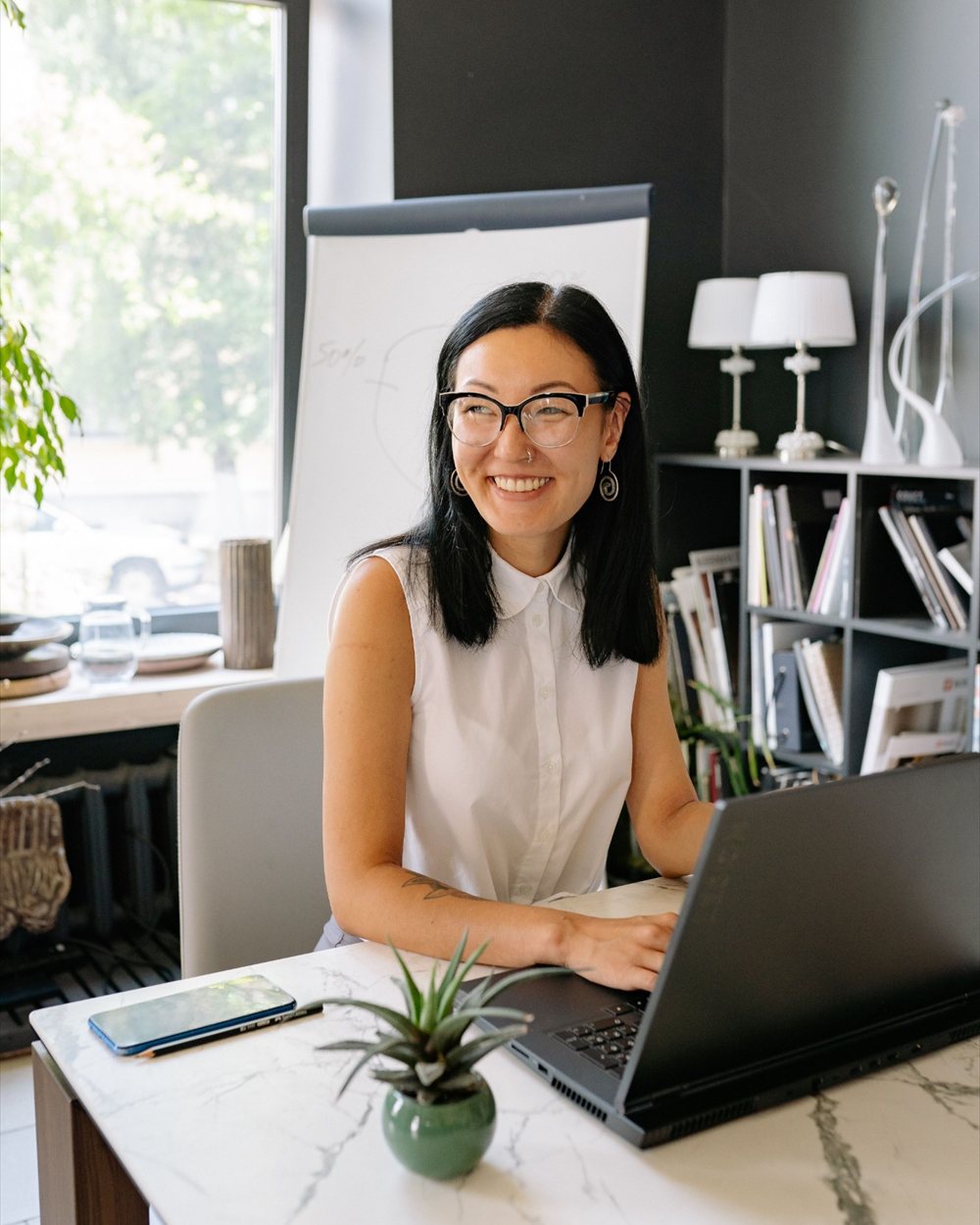 An engineer smiling at her desk, working on a laptop